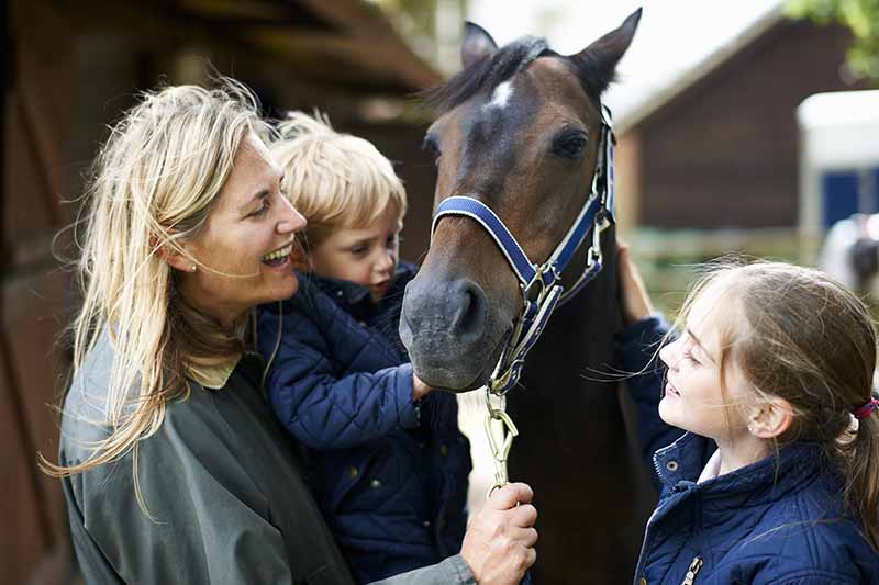 成熟的女人带着儿子和女儿抚摸着马
