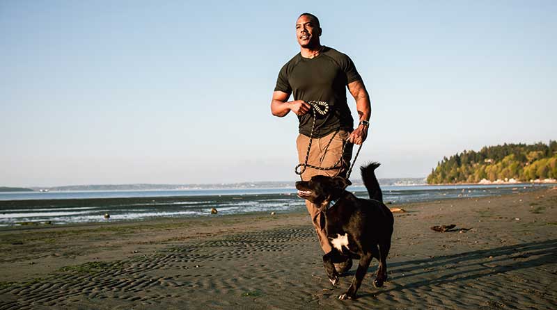 男人带着宠物狗在沙滩上跑步