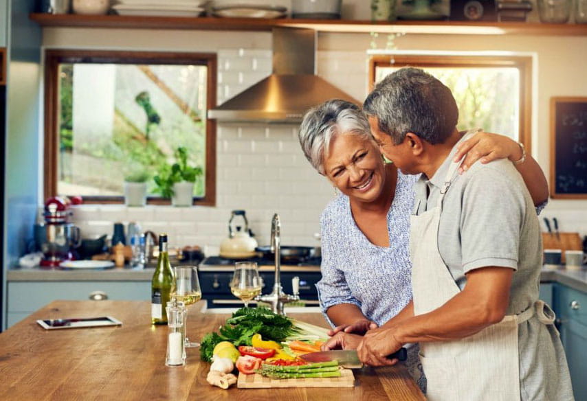 年长的夫妇微笑,一起切蔬菜in kitchen