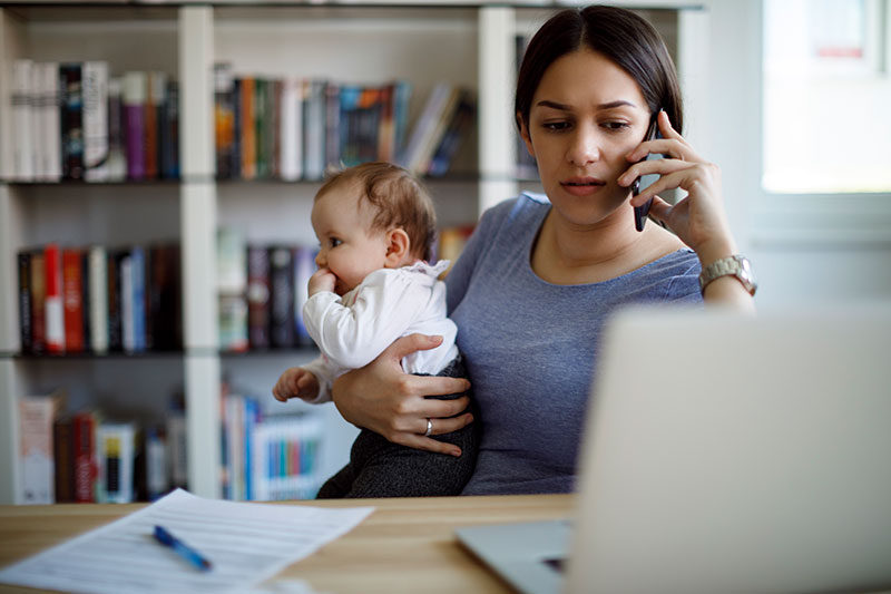 忙着工作的妈妈拿着手机和笔记本电脑抱着宝宝