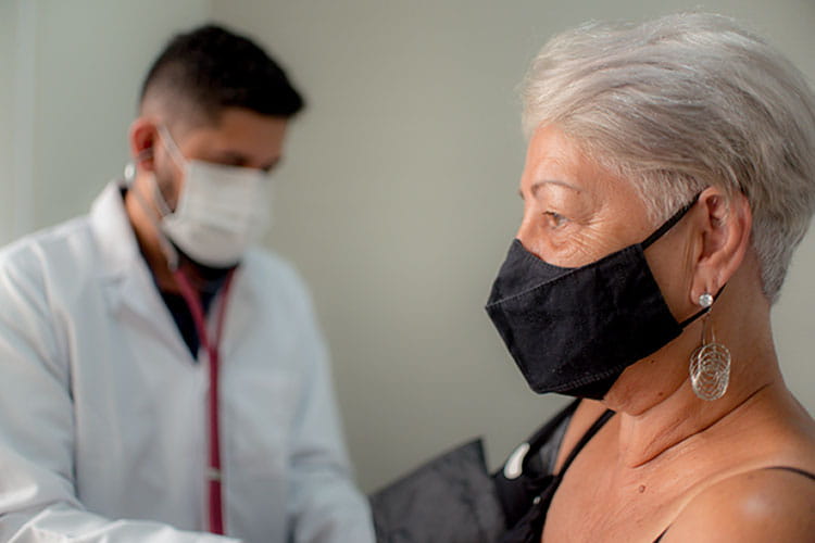 身穿白大褂、戴口罩的男医护人员正在为一名戴黑色口罩的老年妇女检查血压。