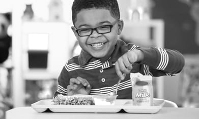 小学年龄的黑人男孩，微笑着吃学校午餐