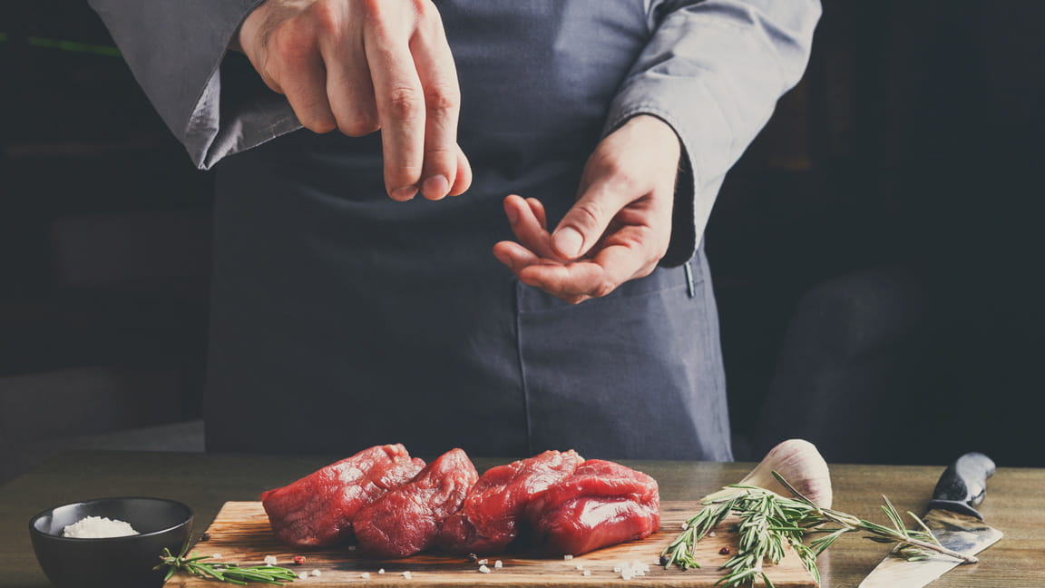 在烹饪时，男人的手在往肉里加盐